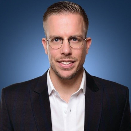 Mann im Anzug mit Brille vor blauem Hintergrund.