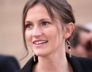 Frau mit braunen Haaren lächelt und trägt große Ohrringe.