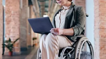 Person im Rollstuhl mit Laptop in einem Büro.