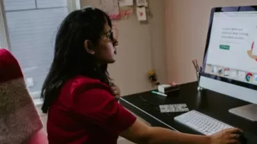 Frau arbeitet am Schreibtisch mit Computerbildschirm.