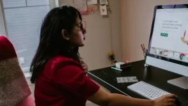 Frau arbeitet am Schreibtisch mit Computerbildschirm.