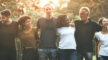 Gruppe von Menschen im Freien, die sich umarmen, lächelnd im Sonnenlicht.