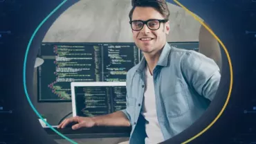 Mann mit Brille sitzt vor zwei Bildschirmen mit Code