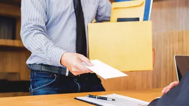 Mann überreicht Umschlag an sitzende Person.