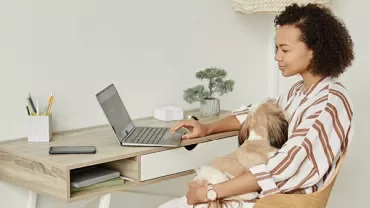 Frau arbeitet an einem Laptop und hält einen Hund auf dem Schoß.