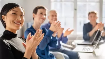 Vier Personen klatschen und lächeln, während sie in einem hellen Büro sitzen. 
