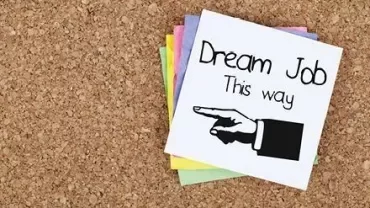 Notiz mit der Aufschrift 'Dream Job this way' und einem Pfeil nach rechts zeigt auf einem Korkbrett.