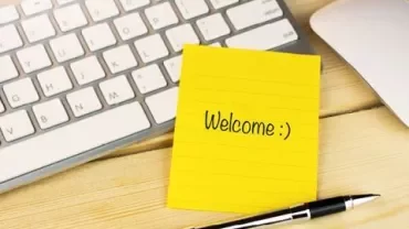 Gelber Notizzettel mit 'Welcome :)' neben einer Tastatur