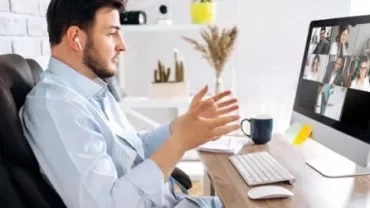 Mann im Videoanruf, gestikulierend, vor Computerbildschirm sitzend.