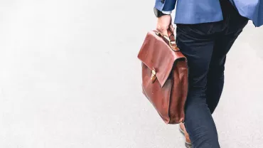 Person in blauer Jacke mit brauner Ledertasche auf der Straße