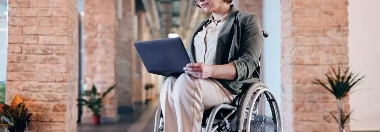 Person im Rollstuhl mit Laptop in einem Büro.