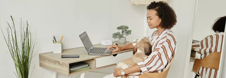 Frau arbeitet an einem Laptop und hält einen Hund auf dem Schoß.