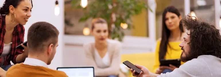 Gruppe von Menschen bei einem Meeting, einer hält ein Handy.