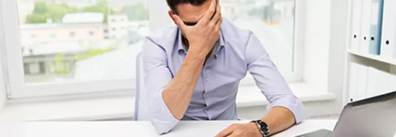 Mann am Schreibtisch hält sich den Kopf in der Hand.
