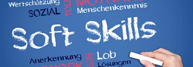 Hand schreibt Soft Skills und Wörter wie Teamwork, Motivation, Respekt auf Tafelhintergrund.