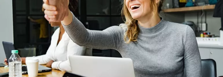 Frau lächelt und gibt einem Arbeitskollegen die Hand im Büro.
