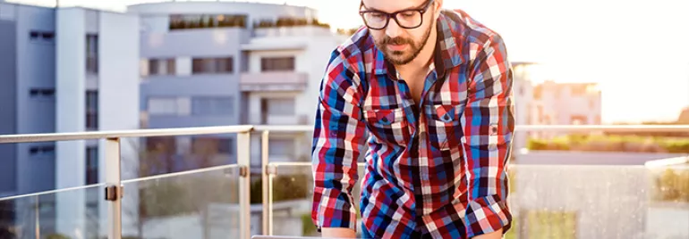 Mann mit Brille arbeitet an einem Laptop auf einem Balkon.