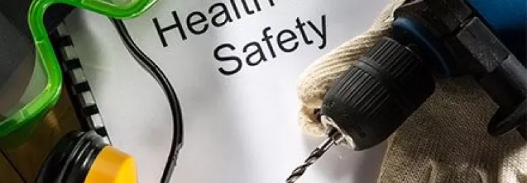 Bohrmaschine, Schutzbrille, Handschuhe und Papier mit 'Gesundheit und Sicherheit'.