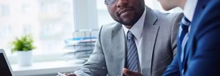 Zwei Männer in Business-Anzügen führen ein Gespräch am Tisch.