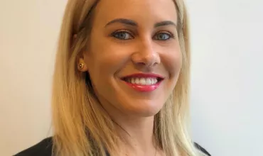 Frau mit blonden Haaren und gelbem Oberteil lächelt