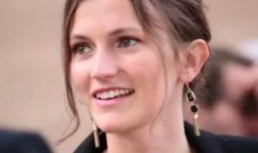 Frau mit langen Ohrringen lächelt und schaut zur Seite.
