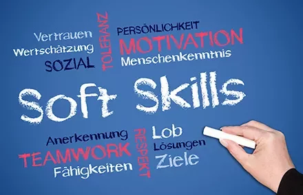 Hand schreibt Soft Skills und Wörter wie Teamwork, Motivation, Respekt auf Tafelhintergrund.