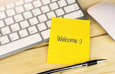 Gelber Notizzettel mit 'Welcome :)' neben einer Tastatur