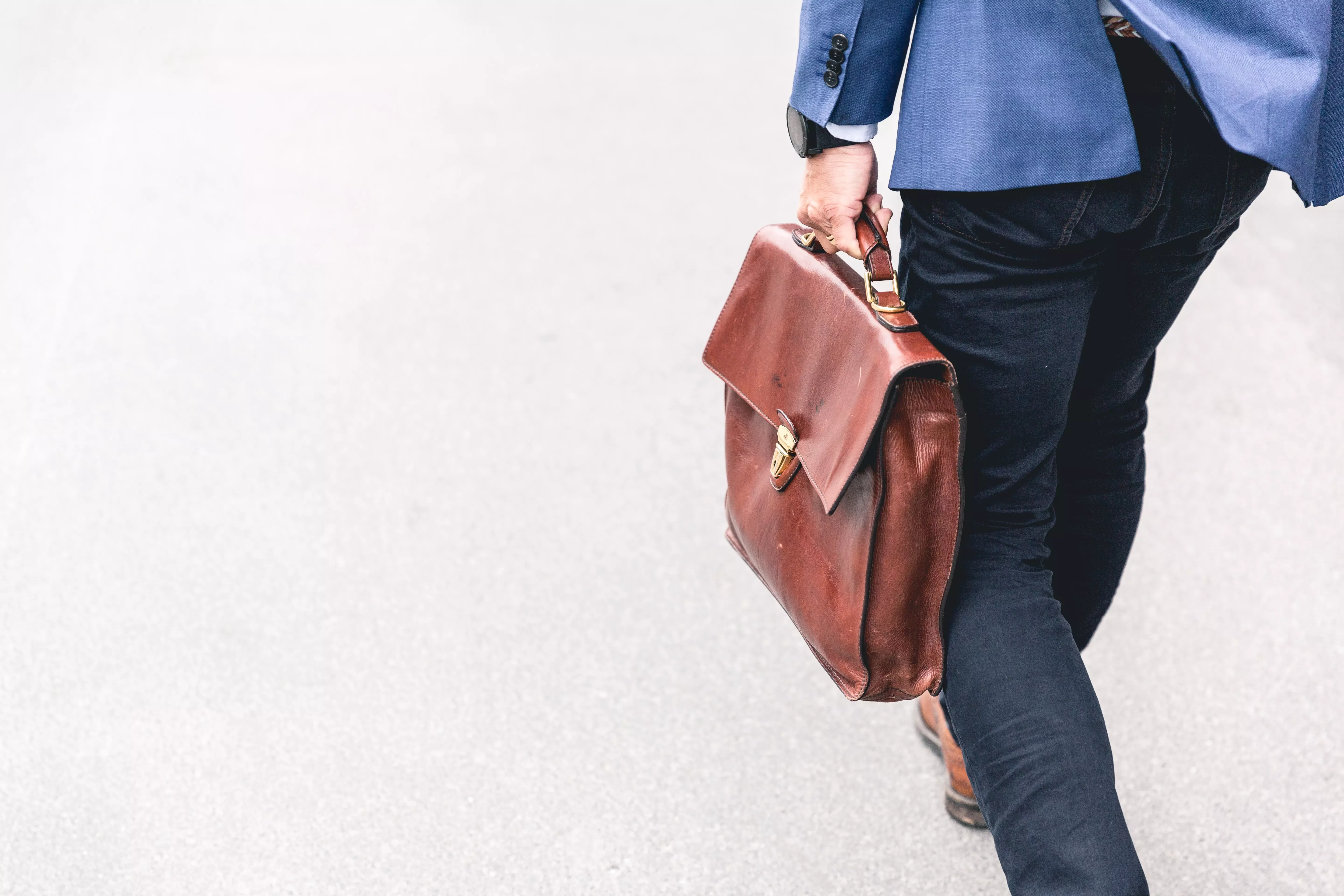 Person in blauer Jacke mit brauner Ledertasche auf der Straße