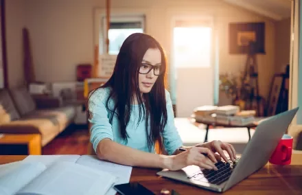 Frau mit Brille arbeitet an Laptop in gemütlichem Wohnzimmer.