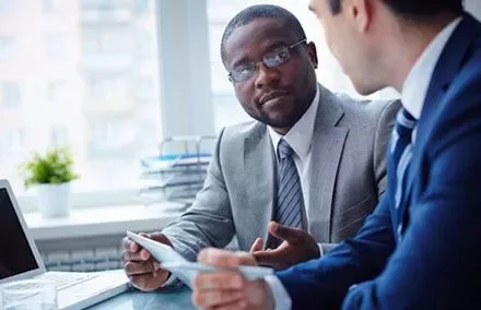 Zwei Männer in Business-Anzügen führen ein Gespräch am Tisch.